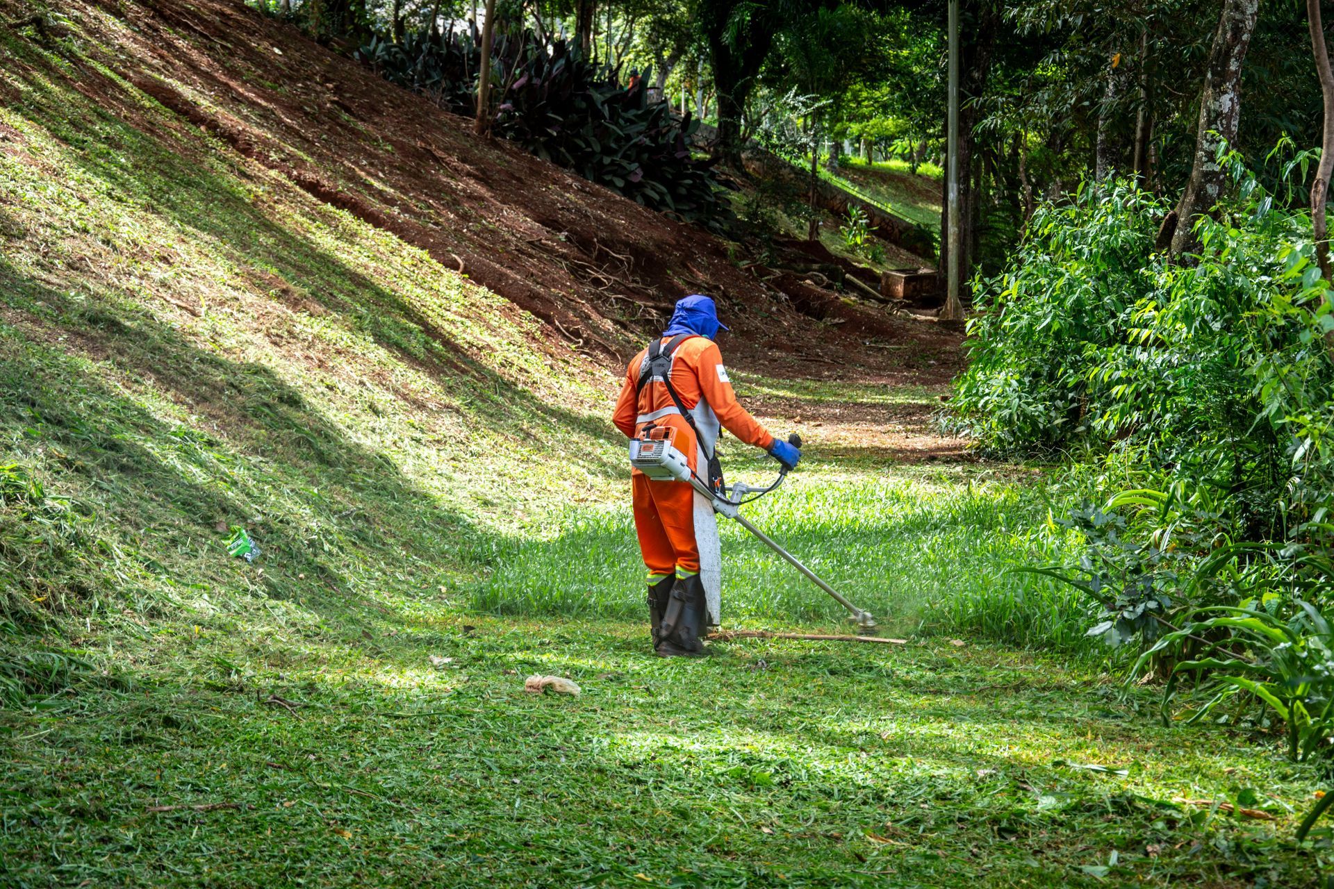A man is cutting grass with a lawn mower in a park.