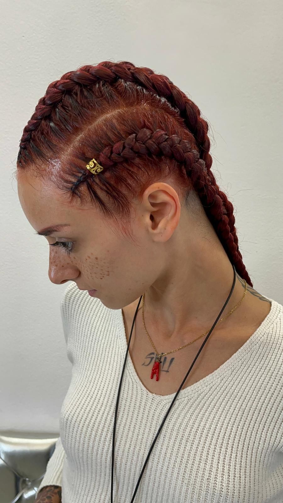 Una donna con le trecce rosse indossa una camicia bianca e una collana.