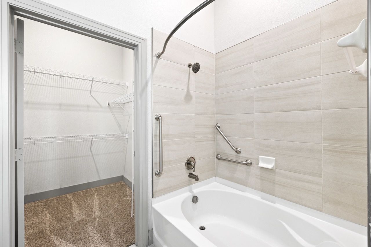 Bathroom with tiled tub/shower, grab bars, and a walk-in closet with wire shelves.