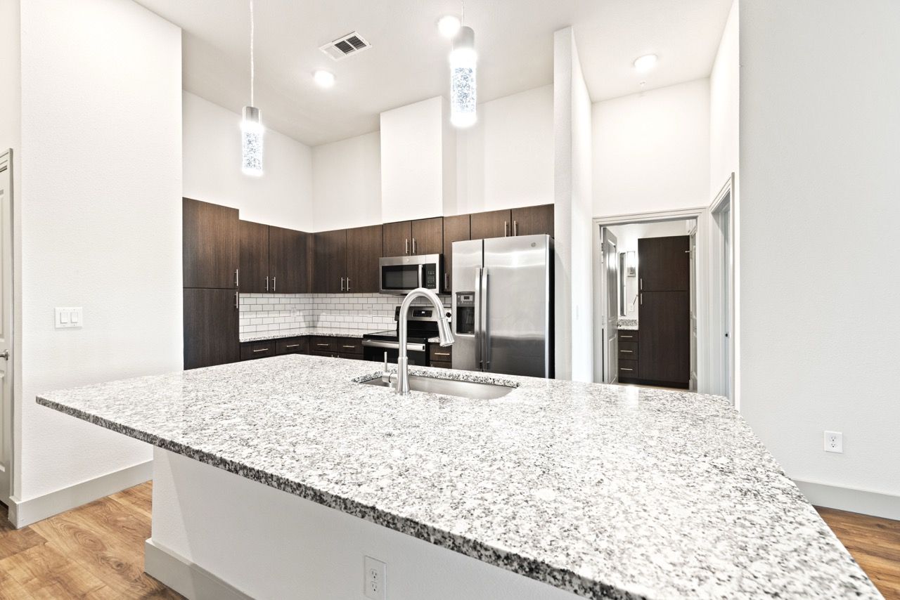 Modern apartment kitchen with granite island, stainless steel appliances, and pendant lights.