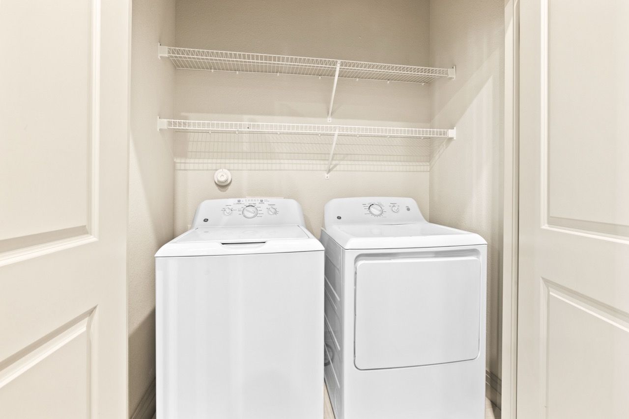 Laundry closet with a washer, dryer, and white wire shelving.