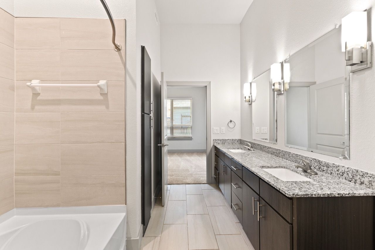 Bathroom with a double vanity, granite countertop, and a tiled tub/shower.