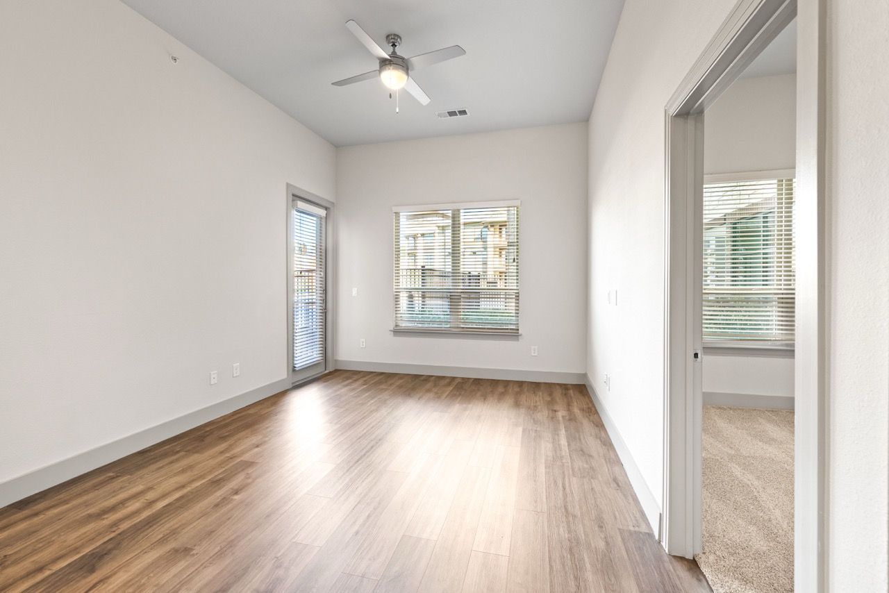 Empty living room with wood-look flooring, a ceiling fan, and large windows.