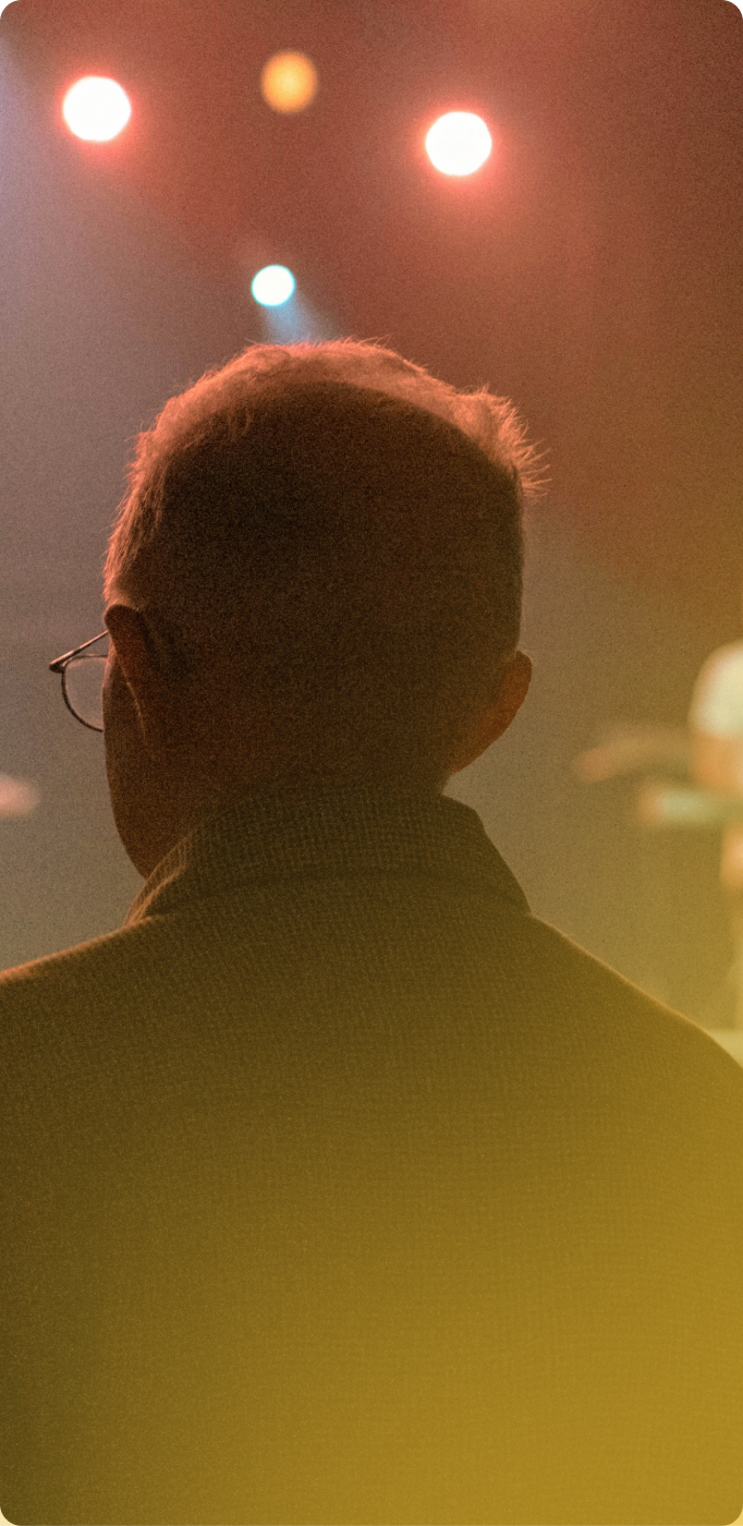 Silhouetted person viewed from behind under colorful stage lights and warm haze