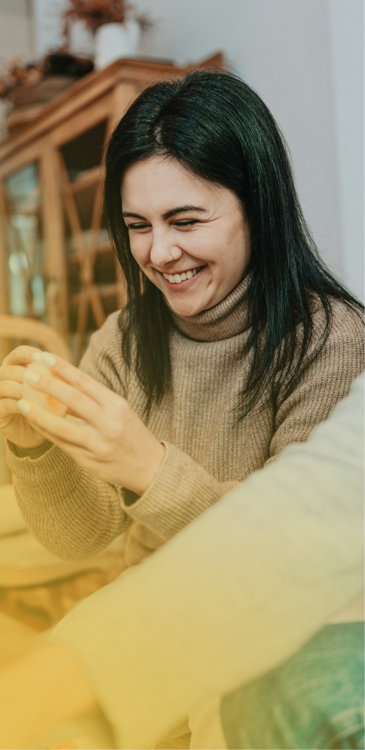 Woman smiling while using a smartphone on a couch in warm indoor light