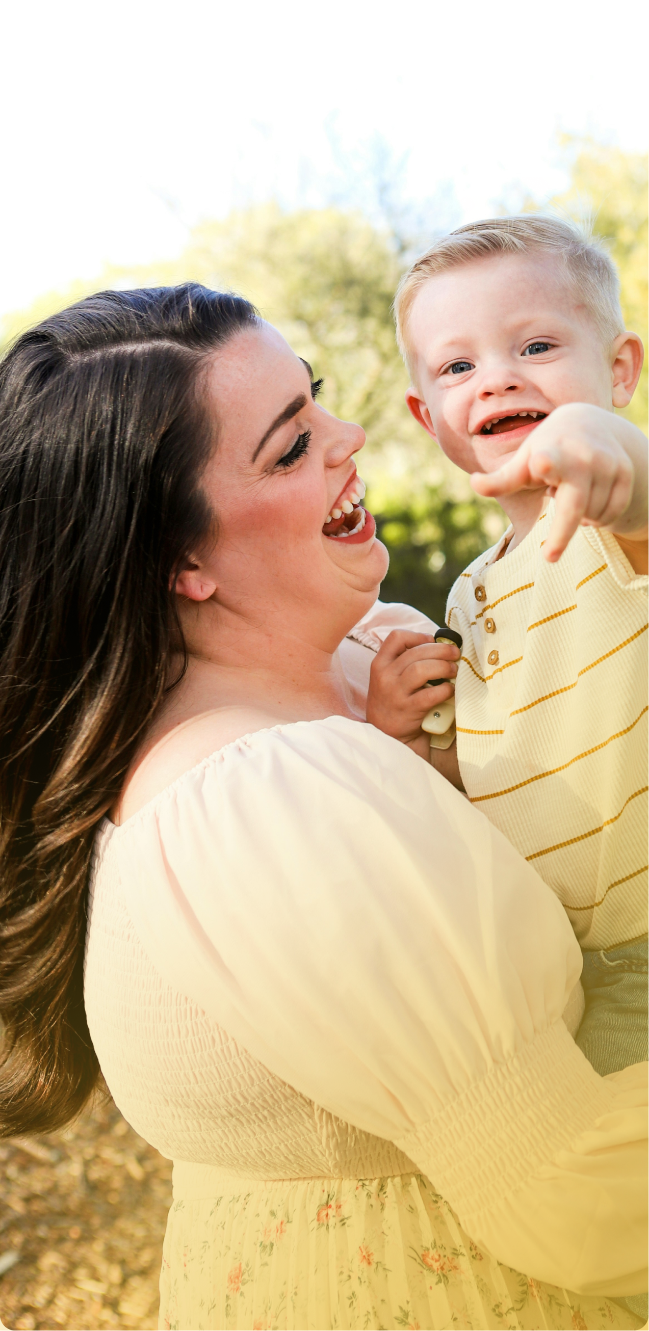 Woman holding smiling baby outdoors in soft yellow clothing