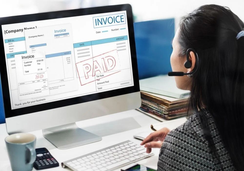 Person at desktop computer viewing an online invoice marked “PAID” on the screen