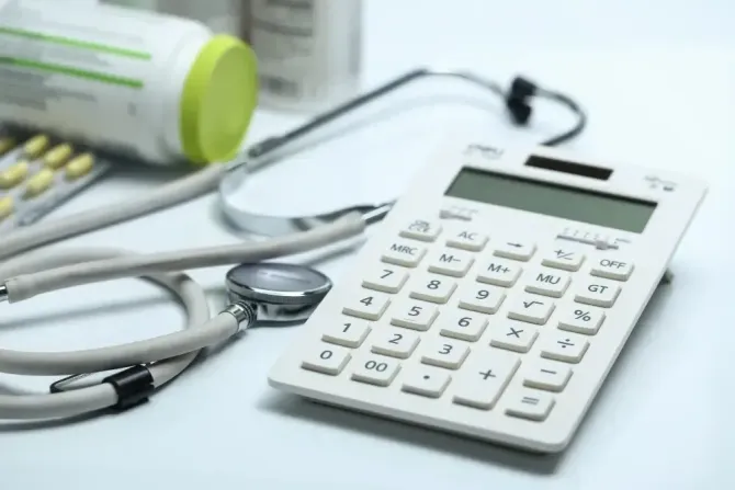 Calculator and stethoscope on a desk with medicine bottles, suggesting medical billing or healthcare finance