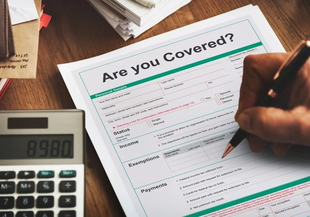 Hand filling out a health insurance form beside a calculator on a desk
