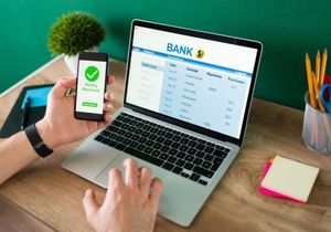 Person using a smartphone to approve online banking on a laptop at a desk