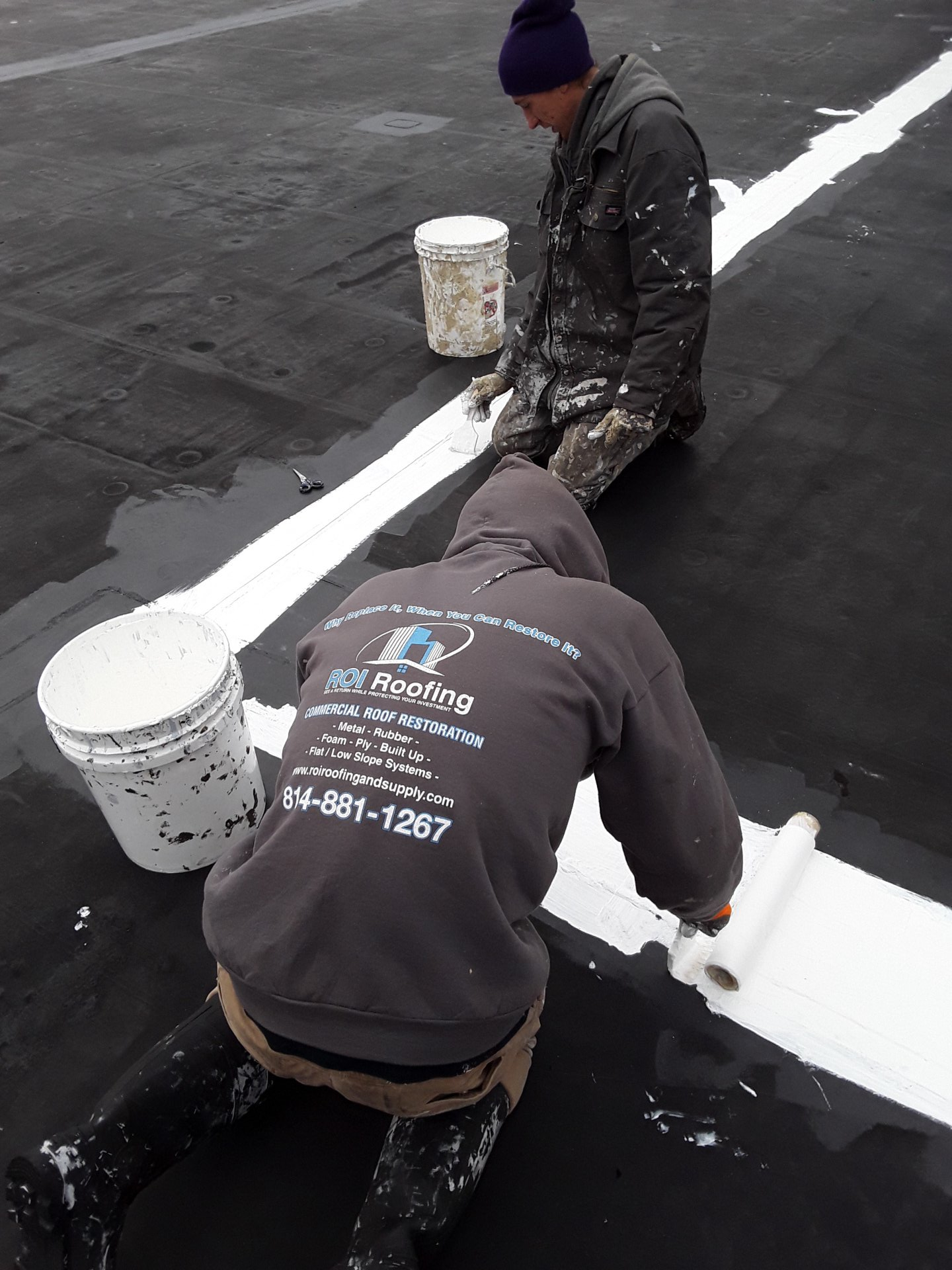 Two men are working on a roof with buckets of paint