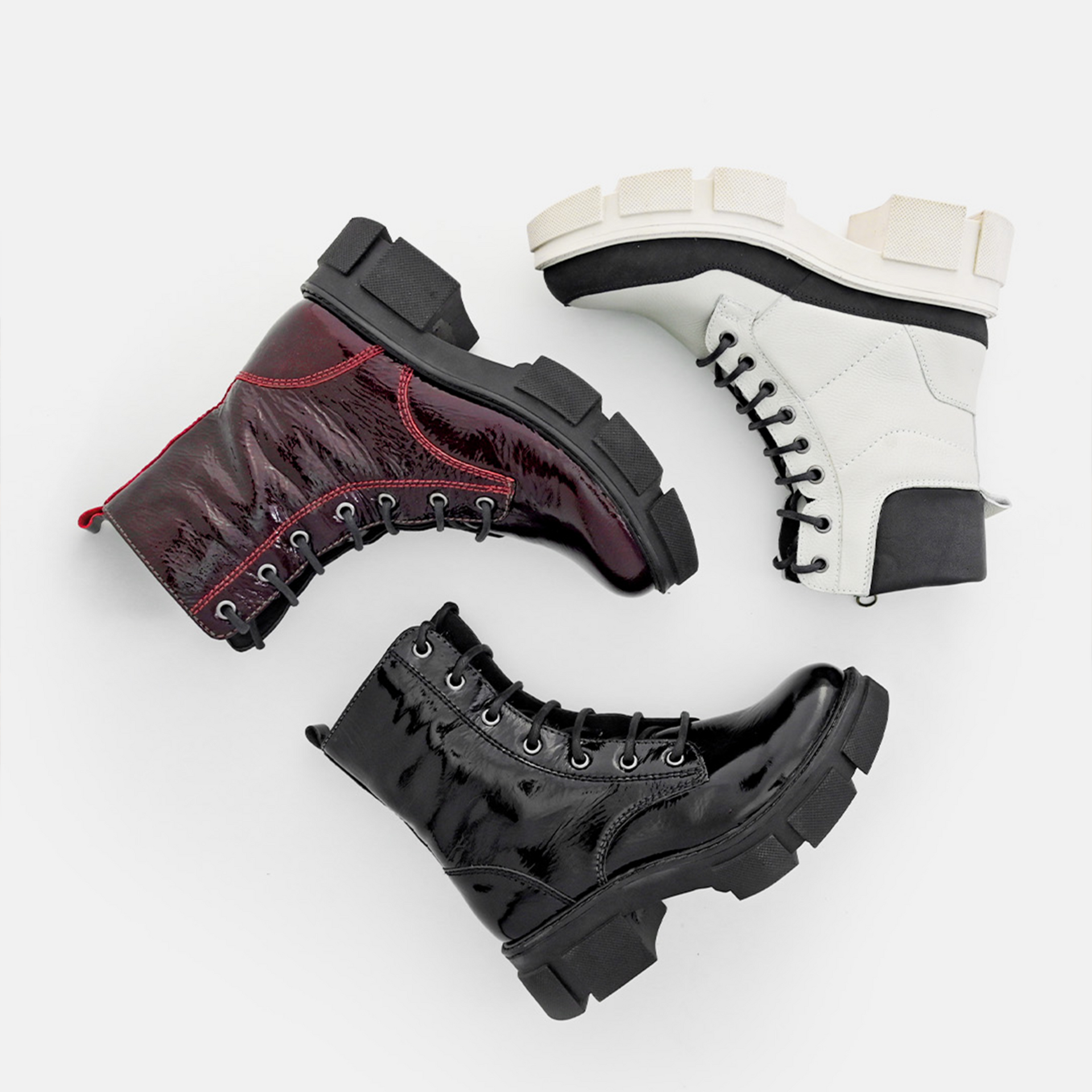 Three chunky lace-up ankle boots in black, white, and black with red accents on a light background