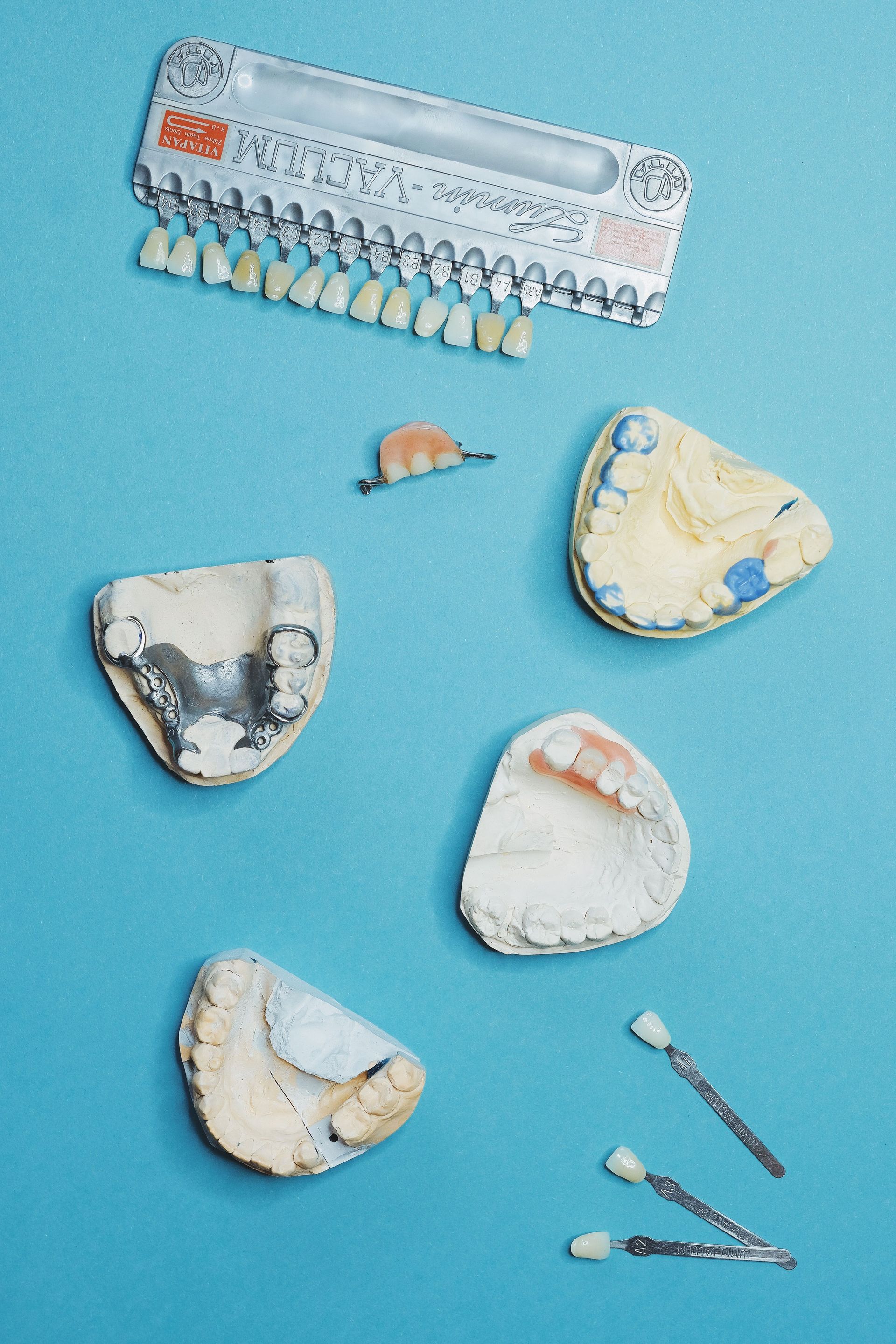 Dental molds and prosthetic teeth arranged on a light blue background with small tools nearby