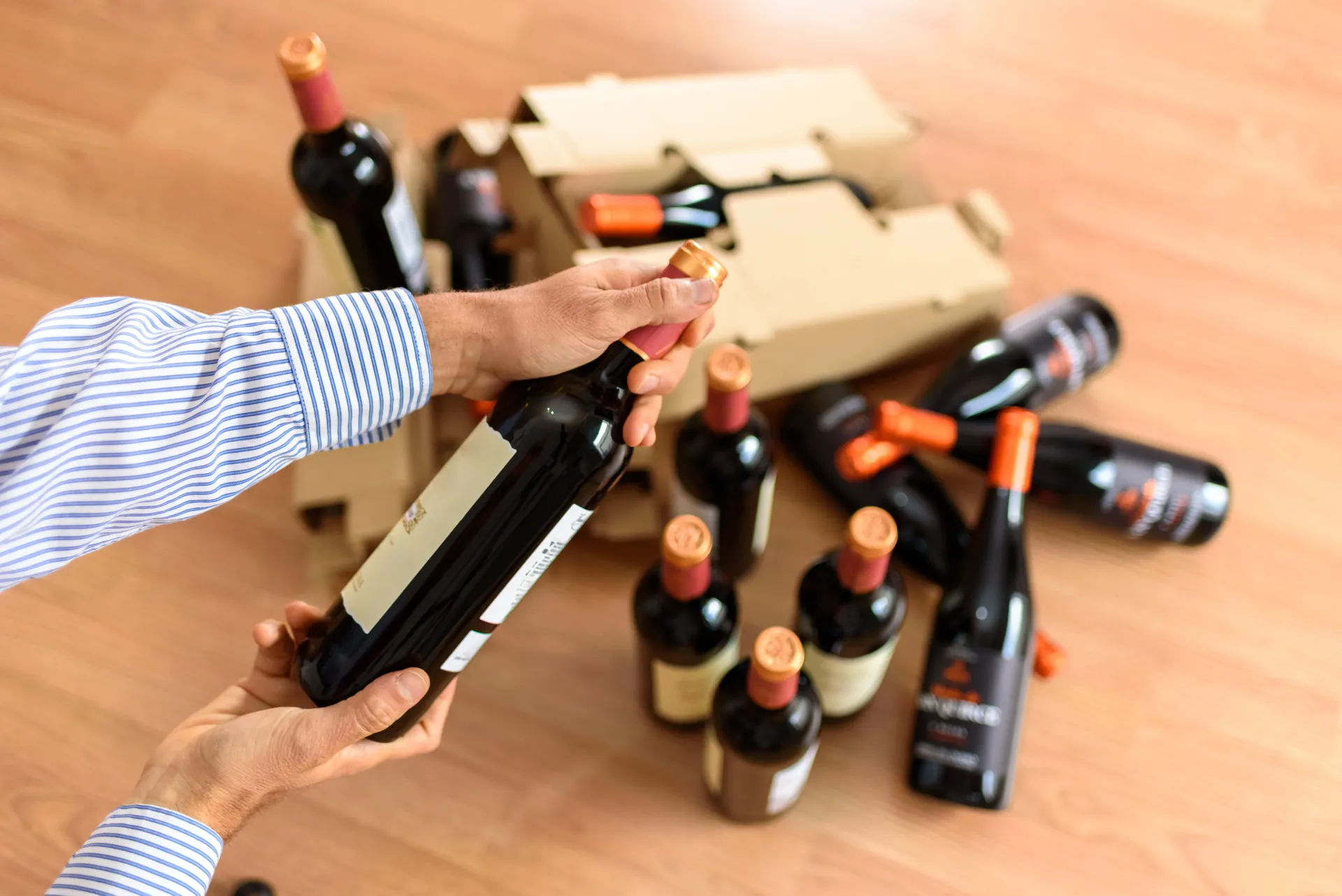 Una persona tiene in mano una bottiglia di vino davanti a una scatola di bottiglie di vino.