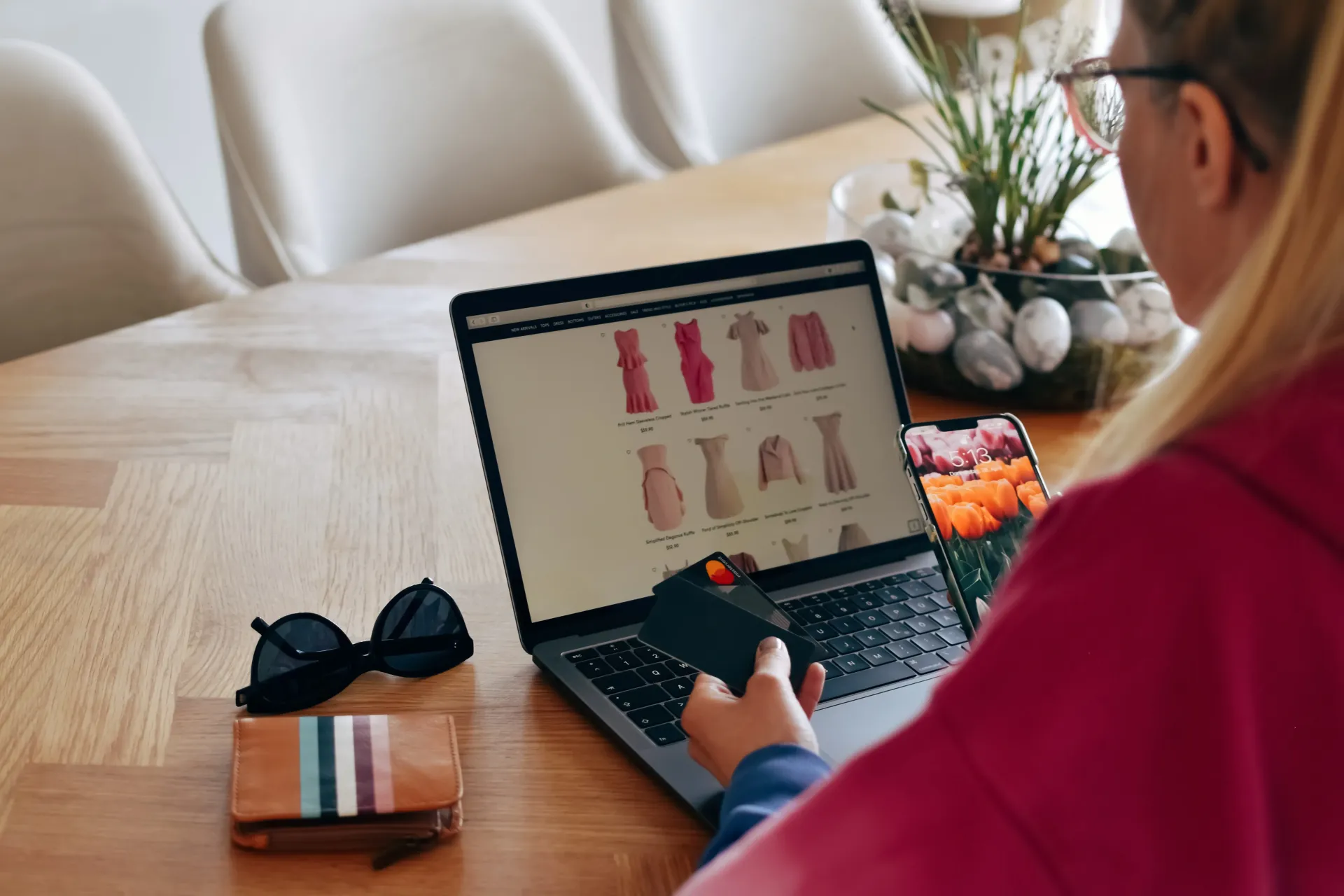 Una donna è seduta a un tavolo e usa un computer portatile mentre tiene in mano una carta di credito.