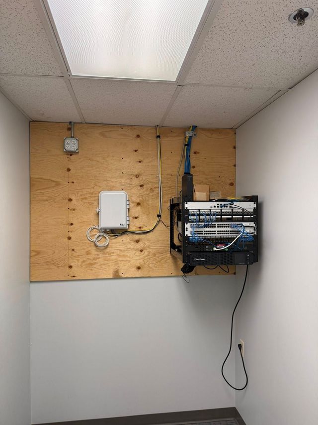 Small utility room wall with mounted networking equipment, cables, and a ceiling light panel.