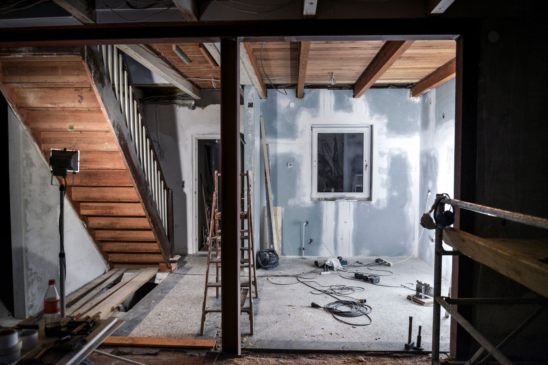 Renovierungsfläche mit freiliegenden Balken, Treppe und einer Fensterwand in einem teilweise fertiggestellten Innenraum