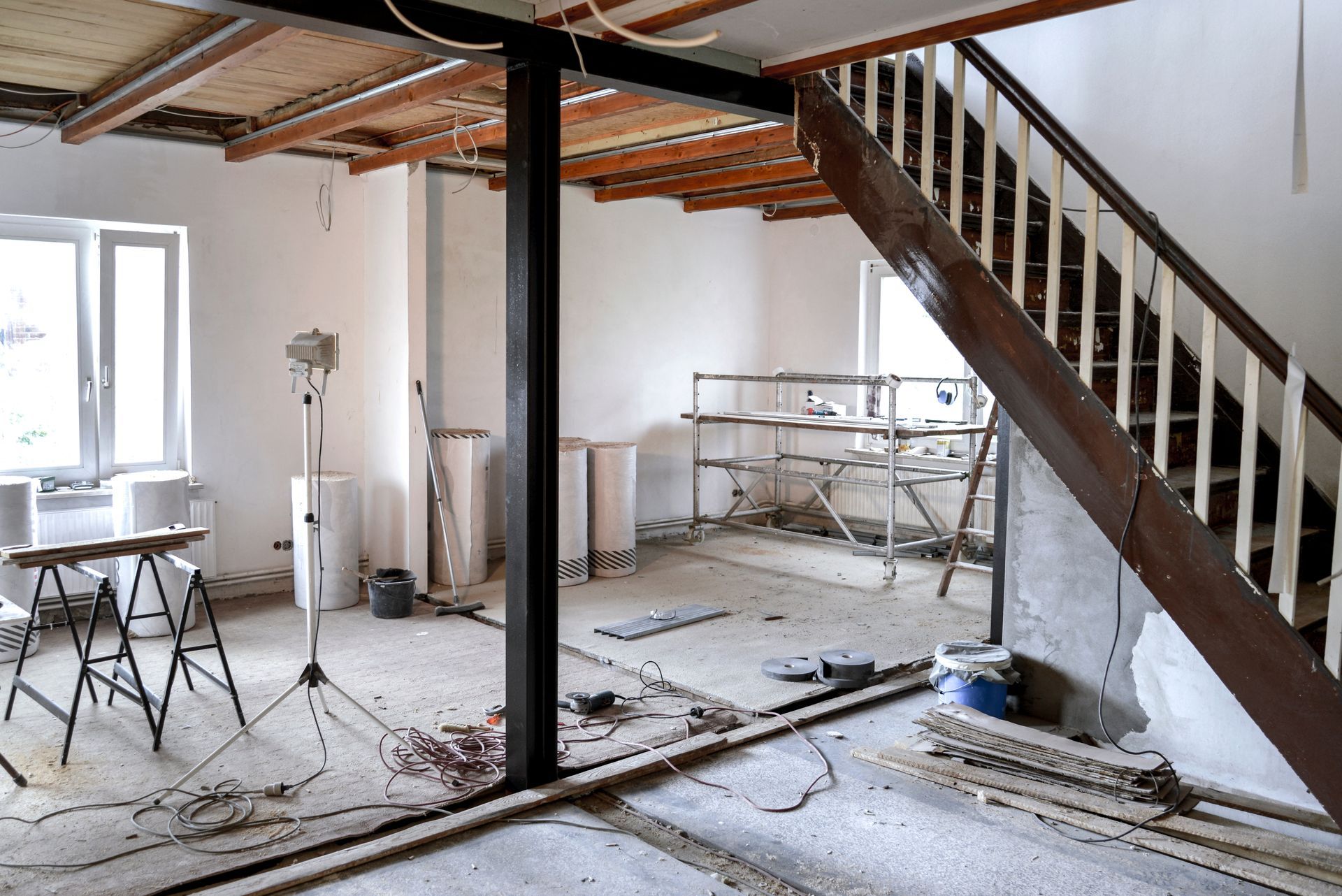 Renovierungsstelle mit freiliegenden Balken, Treppen, Werkzeugen und staubbedecktem Boden in einem Zimmer