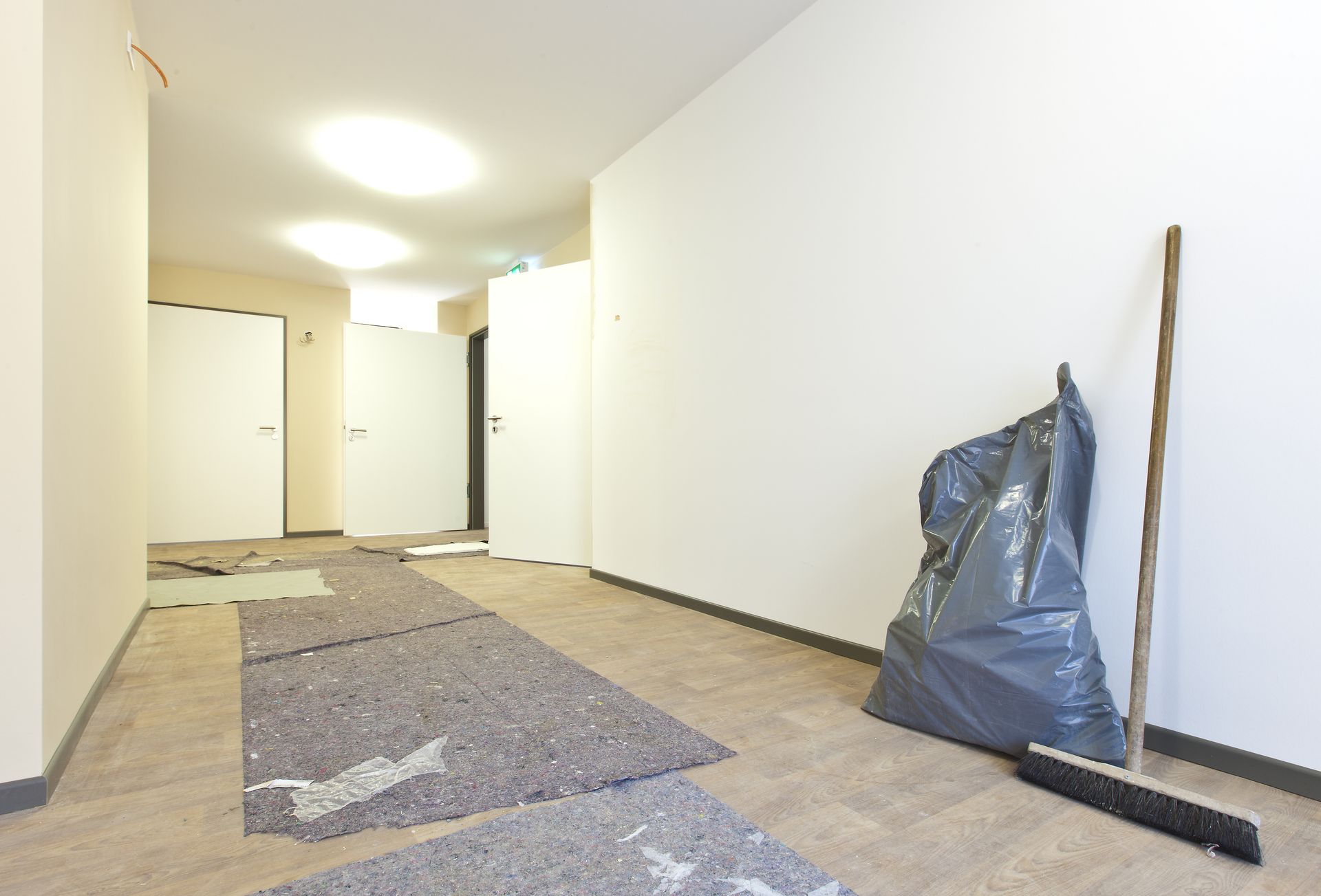 Ein leerer Flur, der gerade renoviert wird, mit Werkzeugen, Abdeckplanen und einem Besen an der Wand.