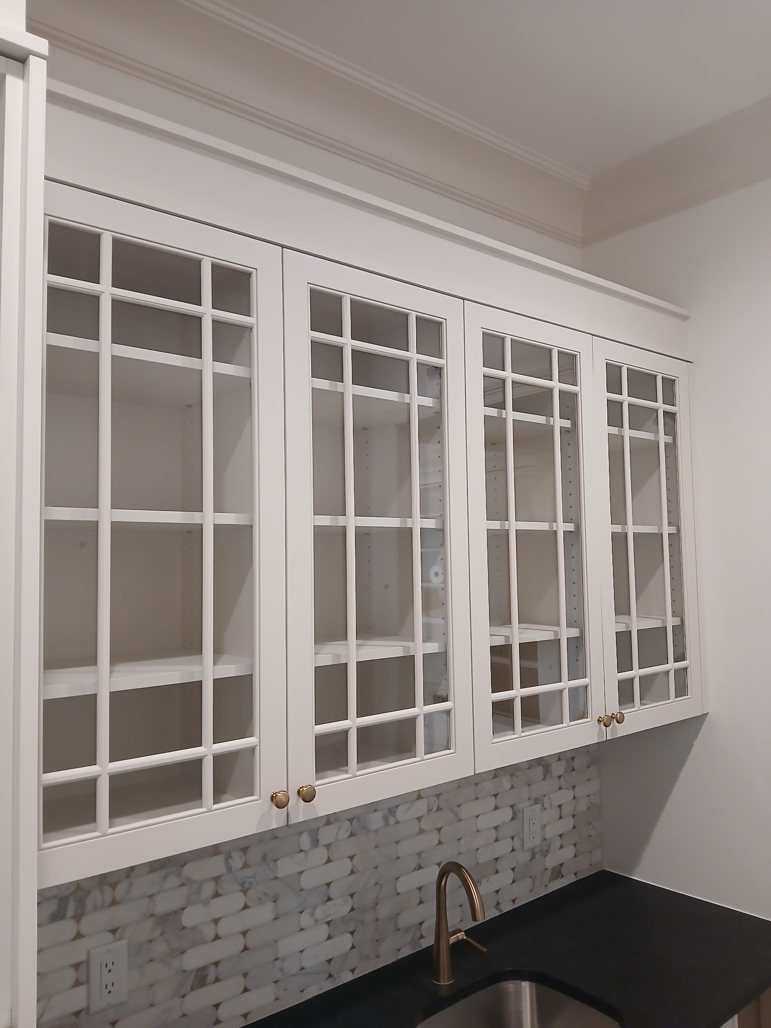 A kitchen with a sink and white cabinets with glass doors