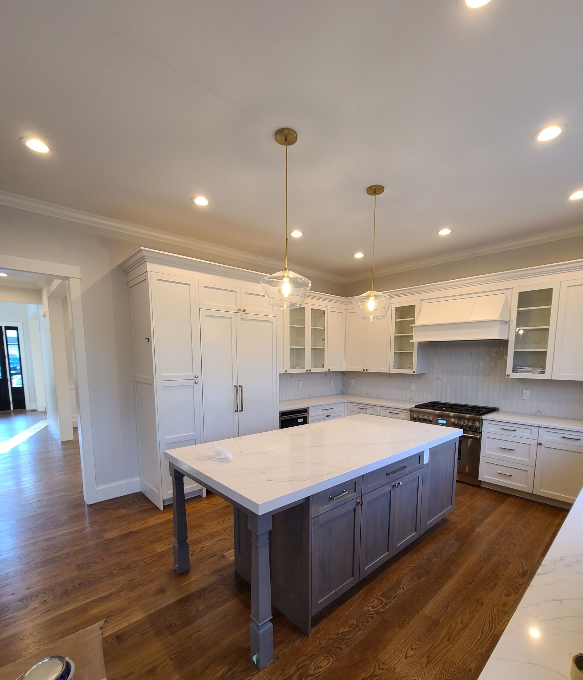 A modern kitchen featuring white cabinets, a grey island with a white countertop, wooden floors, and gold pendant lighting.