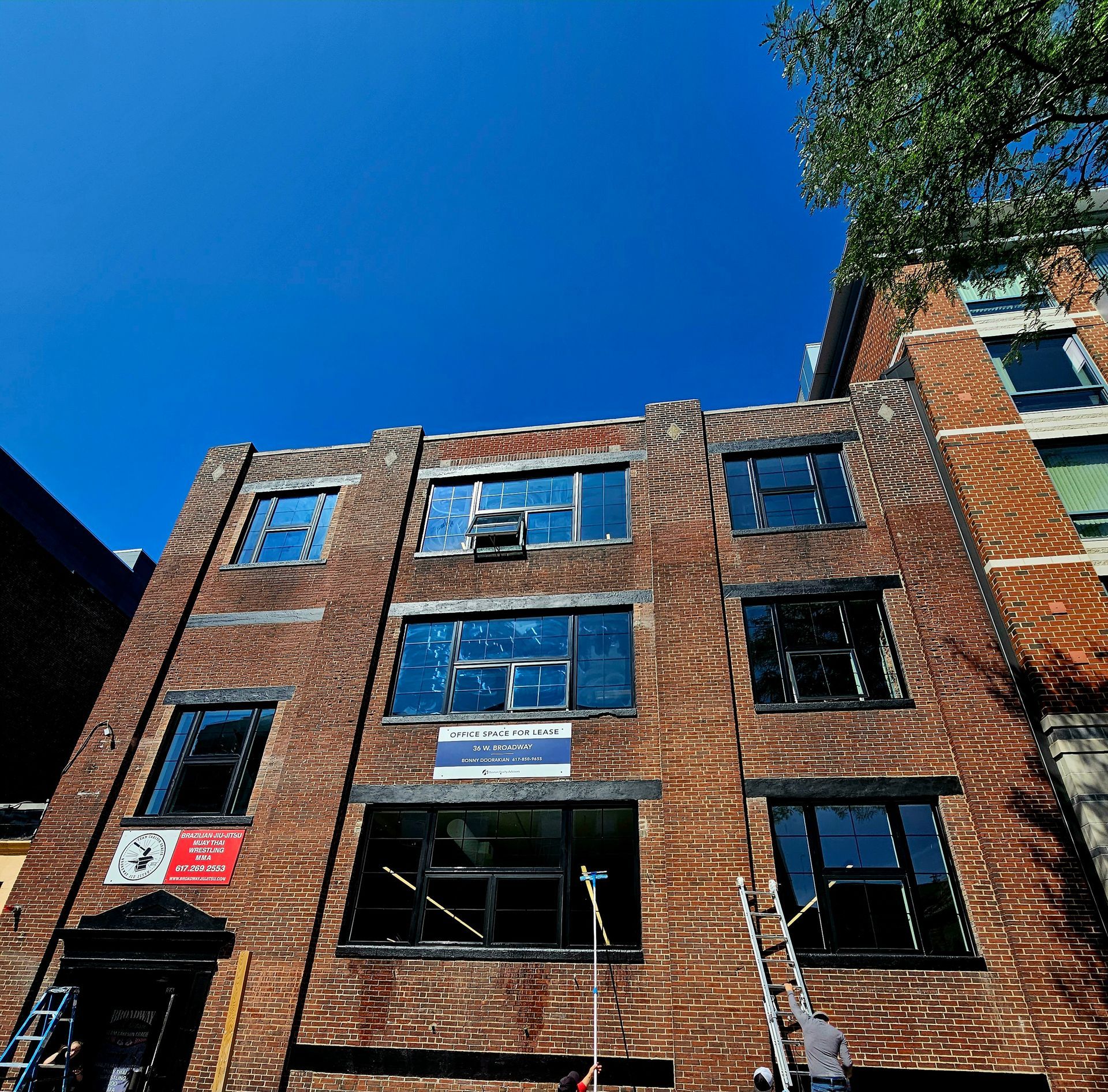 A low-angle view of a brick building with several windows under a clear blue sky, featuring a sign and scaffolding.