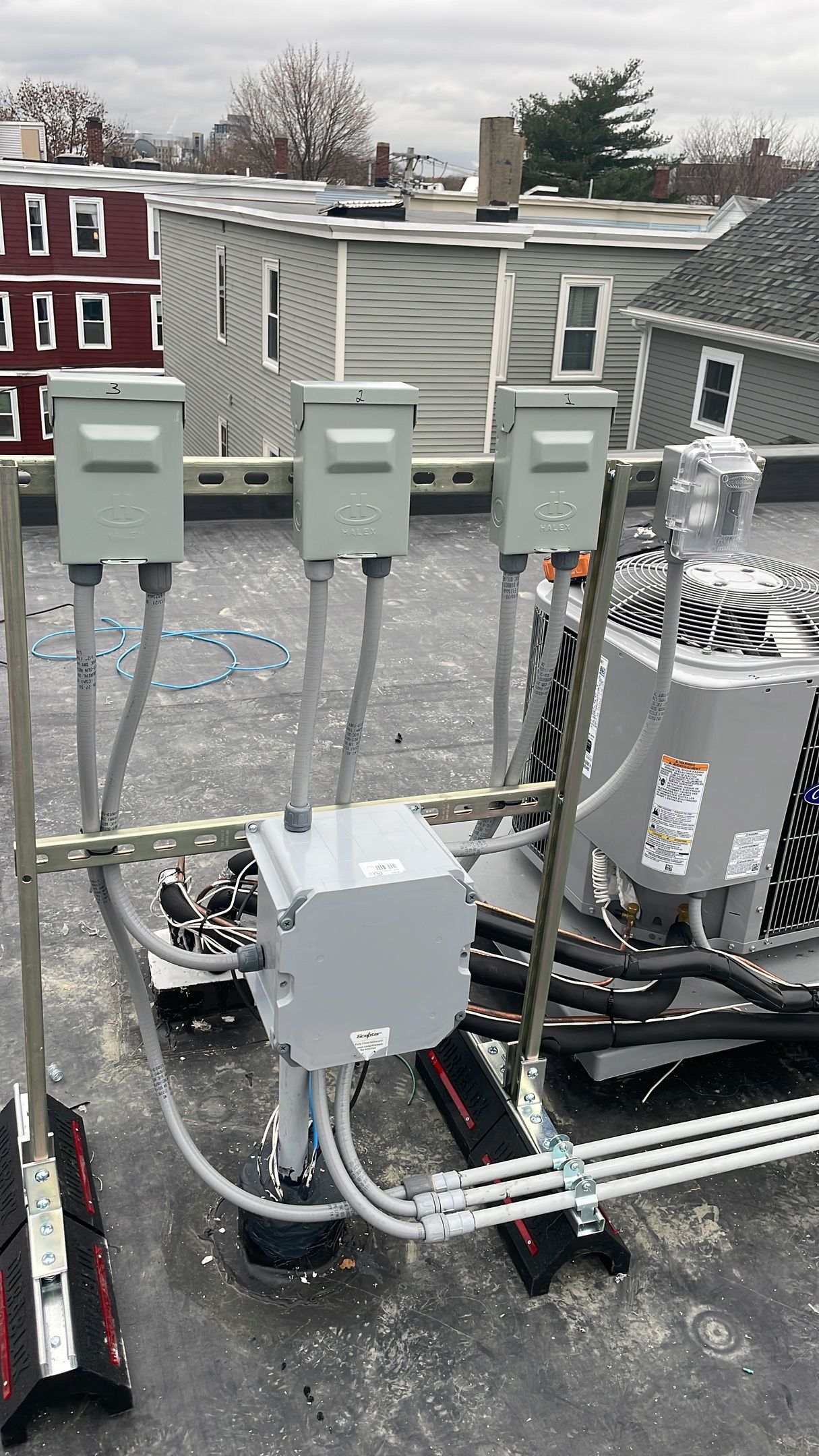Three gray electrical disconnect boxes mounted on a metal frame on a flat rooftop next to an HVAC unit.