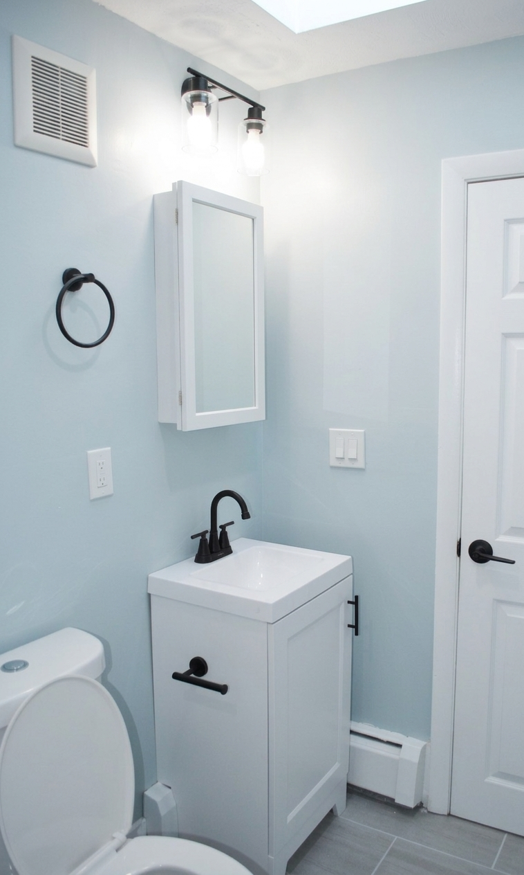 A small bathroom with light blue walls, a white vanity with a black faucet, a white medicine cabinet, and a closed door.