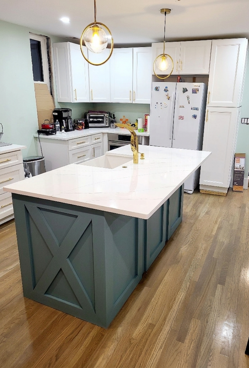 A kitchen with a large blue island, white cabinets, white countertops, two hanging lights, and light wood flooring.