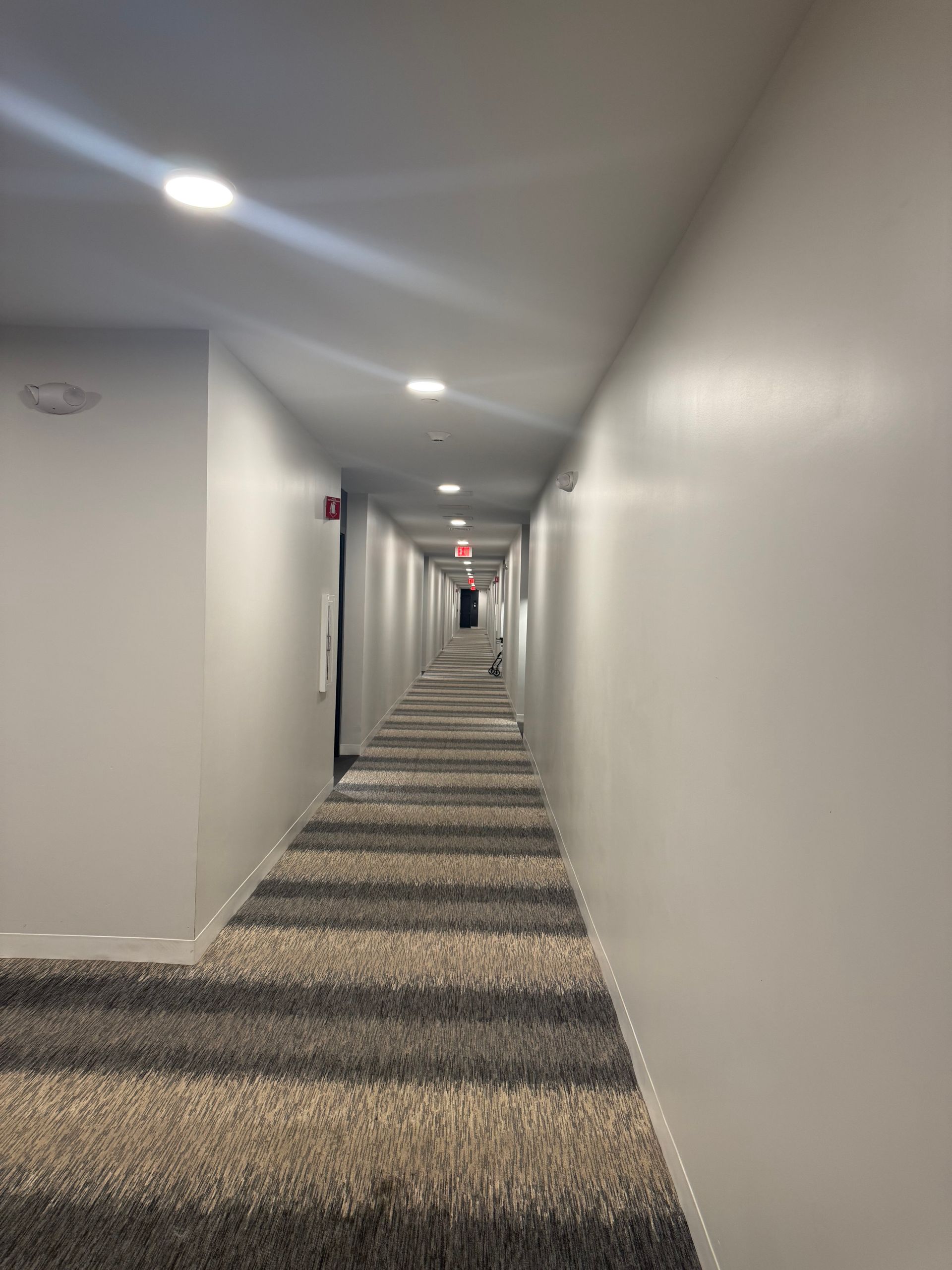 A long, empty indoor hallway with gray walls and a carpet featuring wide, horizontal stripes in shades of gray and beige.