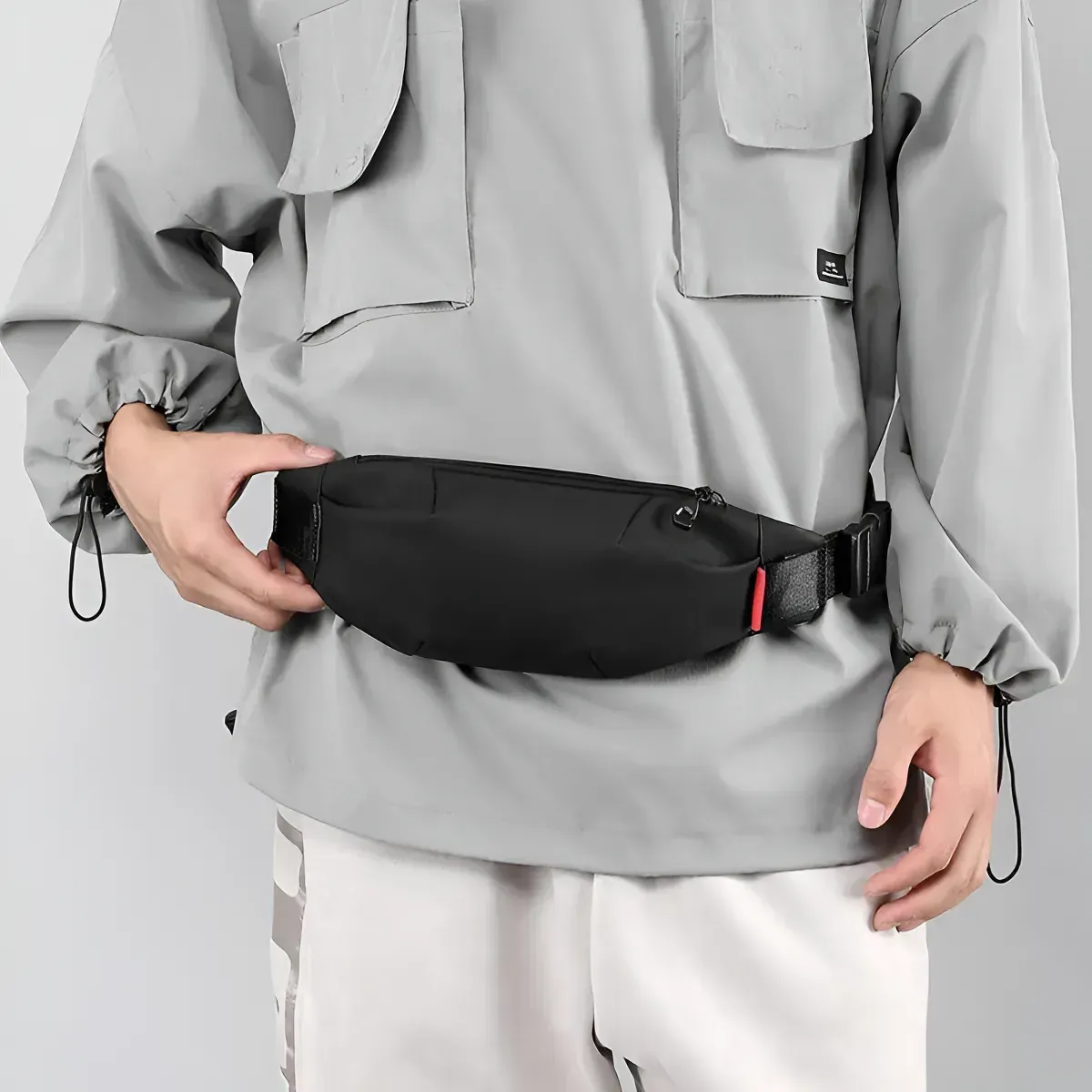 Persona con chaqueta gris y pantalón blanco y riñonera negra.