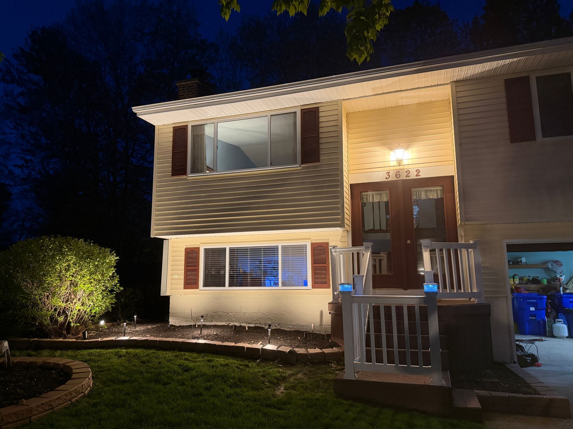Two-story house at night with warm porch lights, front steps, and illuminated windows.