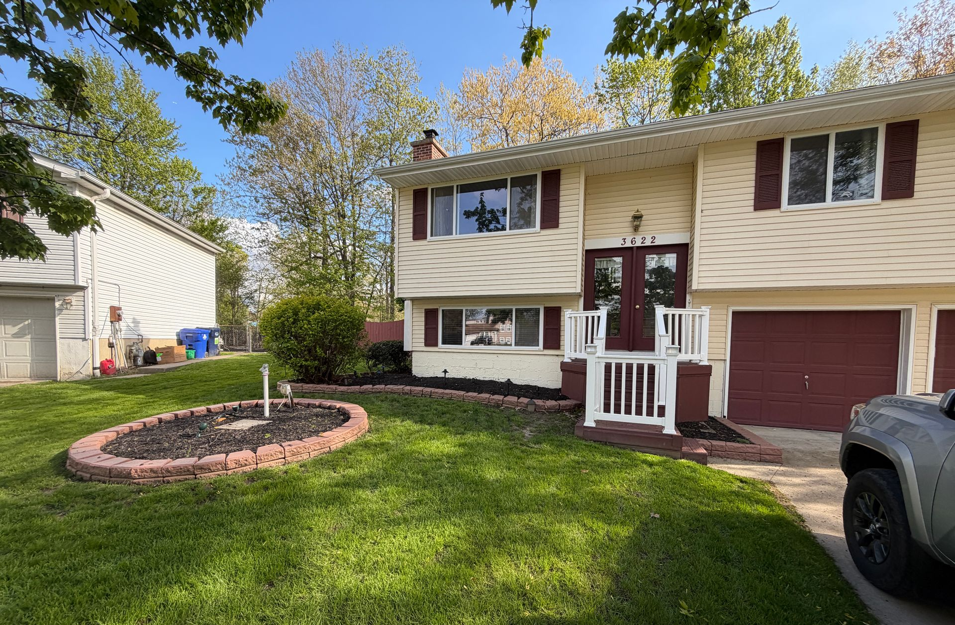 Suburban split-level house with beige siding, red door, front lawn, and circular flower bed.