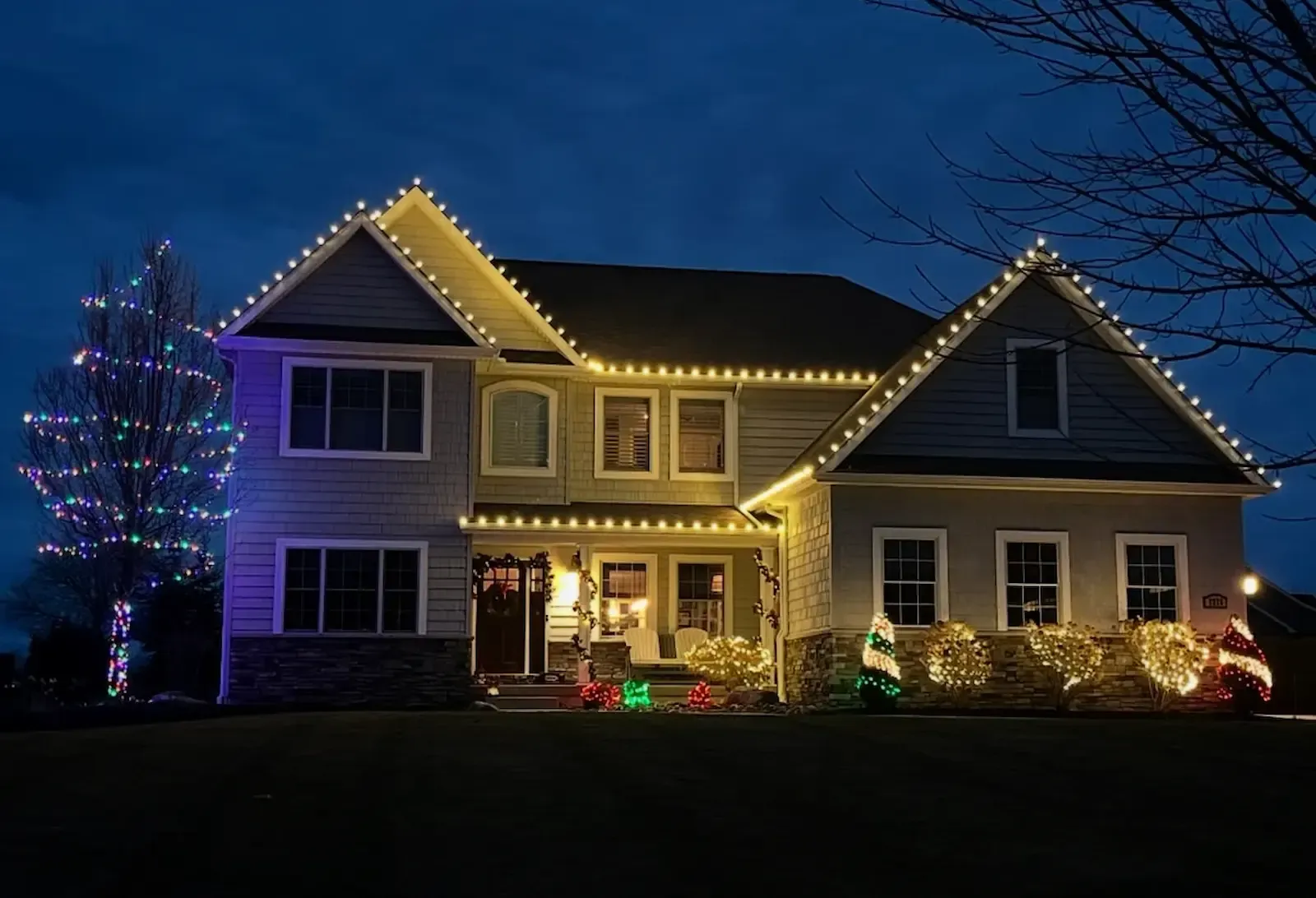 House decorated with landscape lighting, Christmas lights, covered in snow, at night.