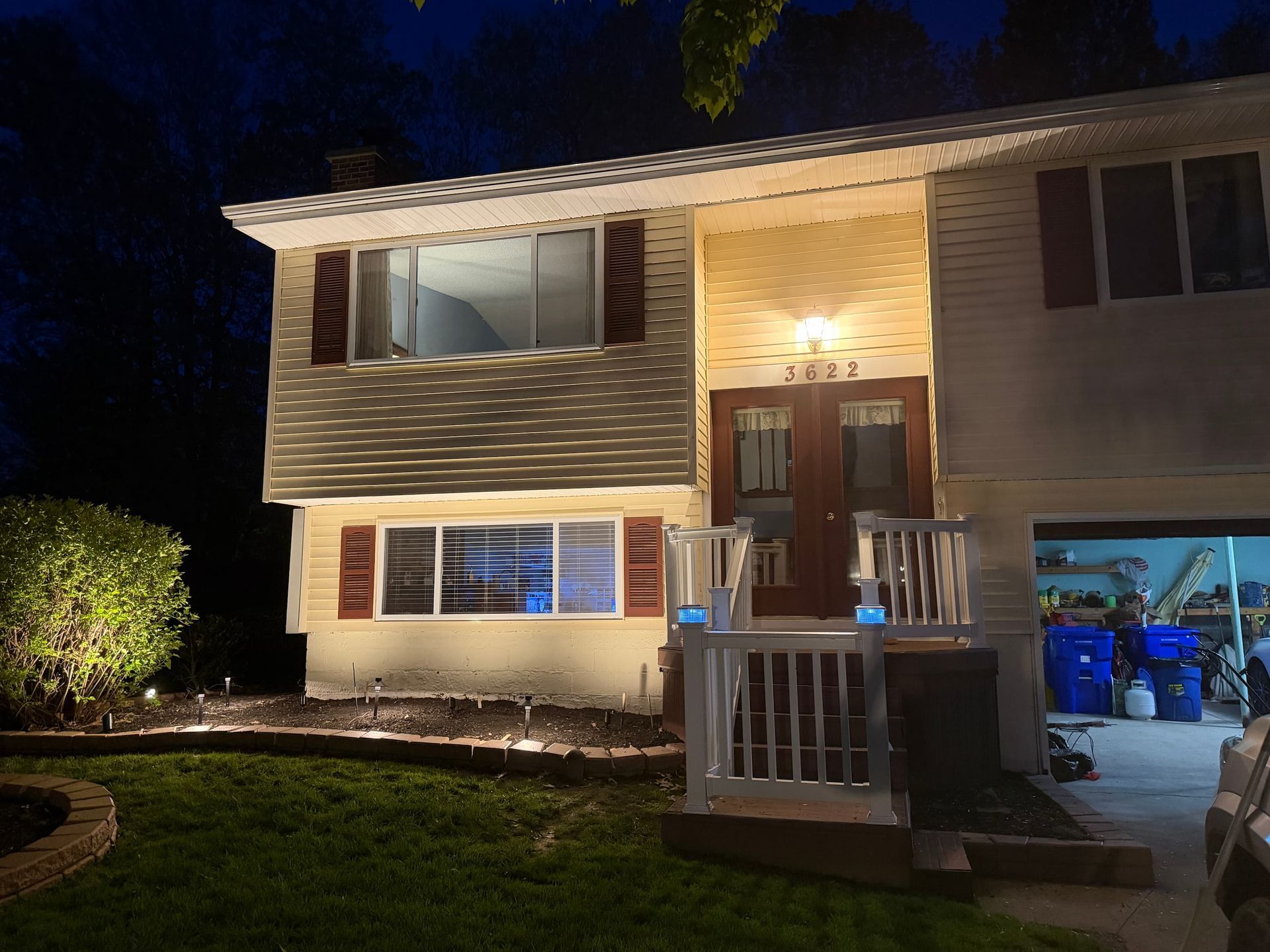 Two-story house at night with porch lights on and an open garage glowing blue inside
