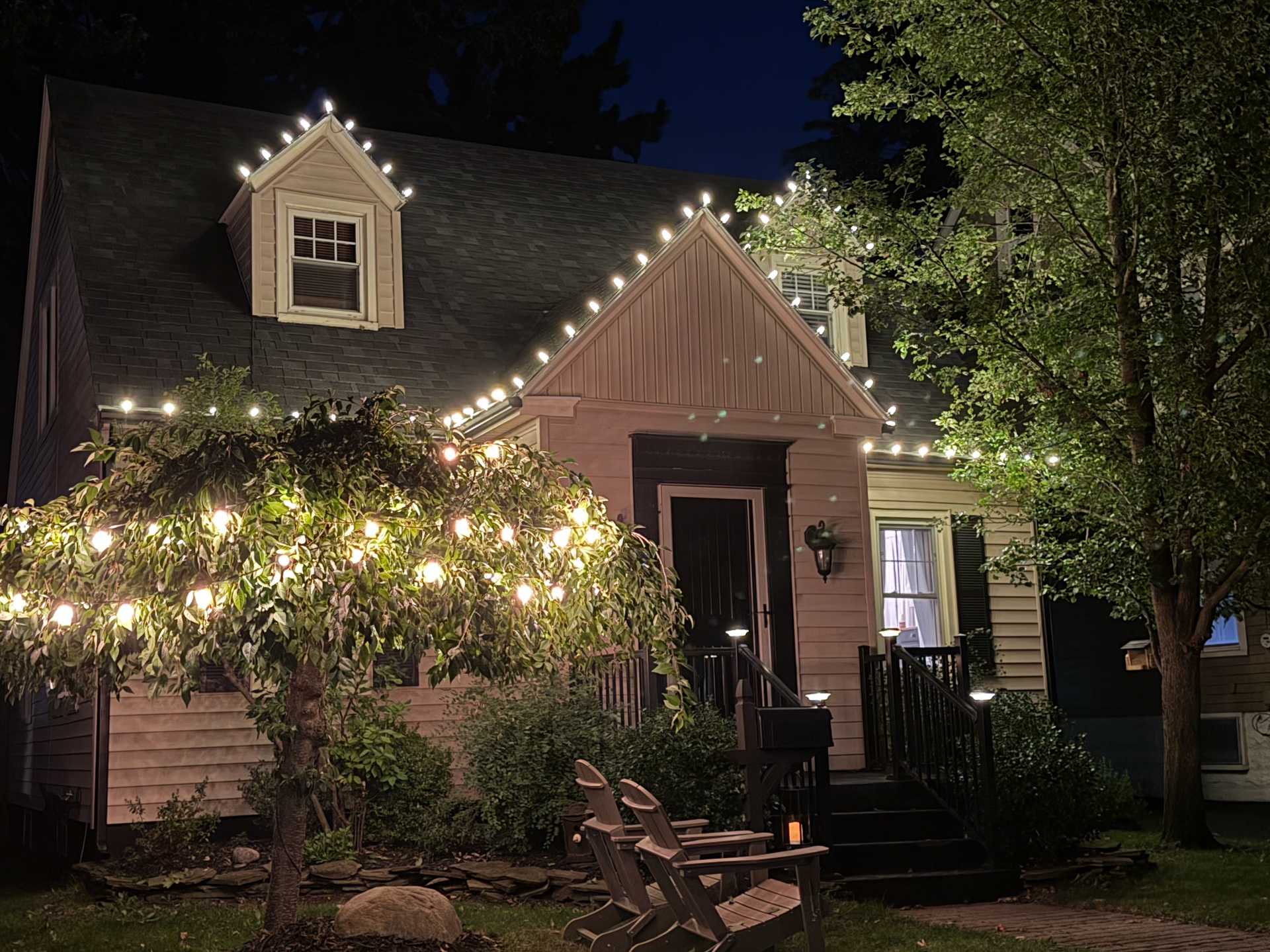 Nighttime cottage with professional warm white holiday lights along the roofline and a small front tree
