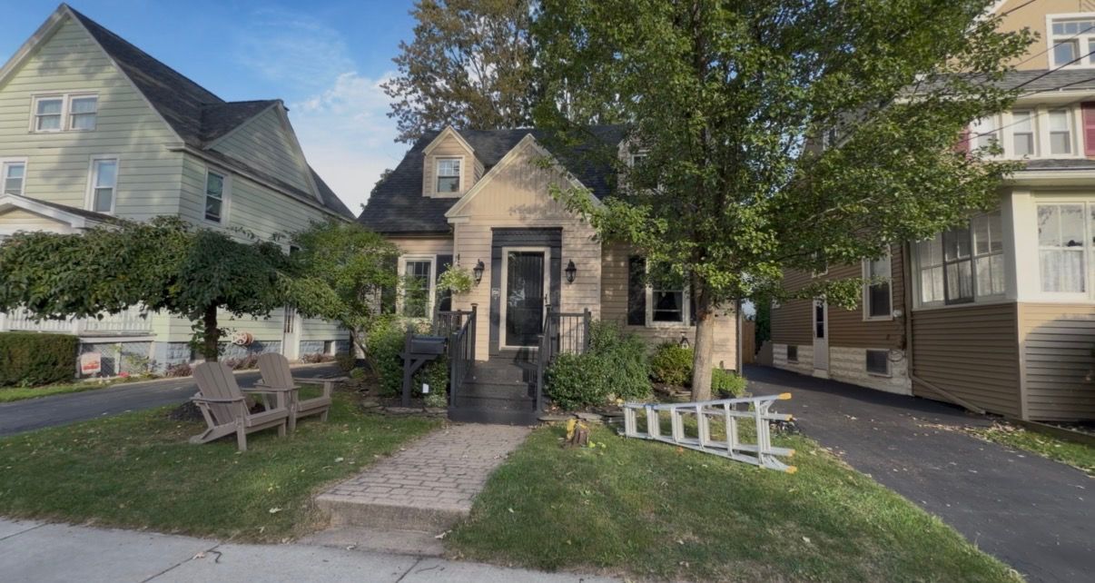 Small front garden and walkway leading to a beige house with benches and trees in a residential neighborhood