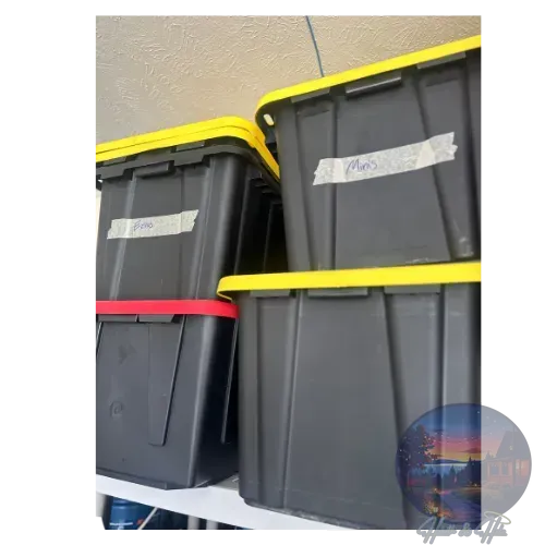 Black storage bins with yellow and red lids stacked on a shelf, labeled with tape.