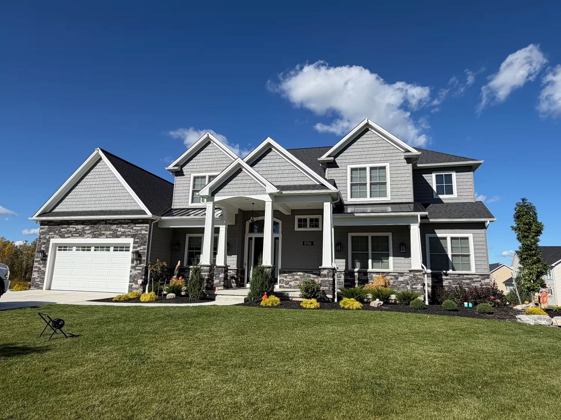 Large gray suburban house with white trim, a front porch, and a green lawn under a blue sky