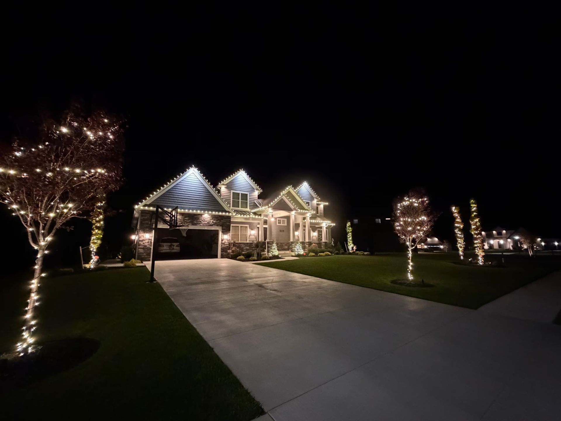 A lit suburban house at night with a decorated driveway and illuminated trees