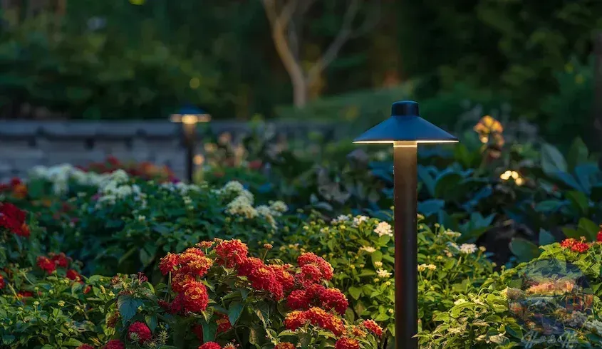 Garden illuminated at dusk with red and white flowers and path lights.