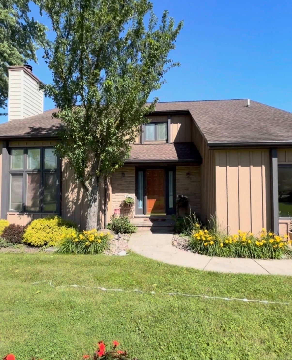 Small front garden and walkway leading to a beige house with benches and trees in a residential neighborhood