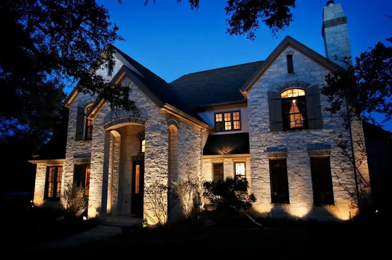 Illuminated stone house at dusk. Outdoor lighting showcases the architecture against a blue sky.