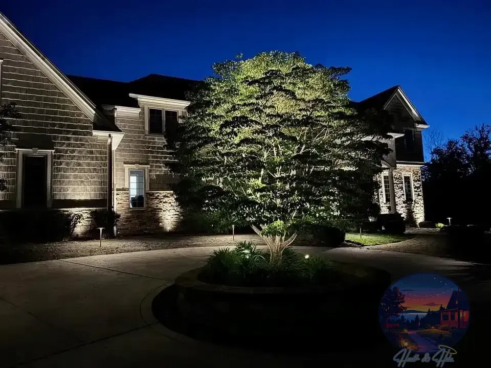 House with outdoor lighting illuminating the facade and a tree in a circular bed on the driveway.