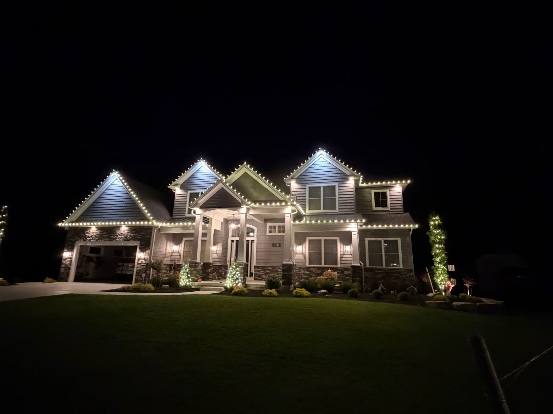 Well-lit suburban house at night with a large lawn and dark sky