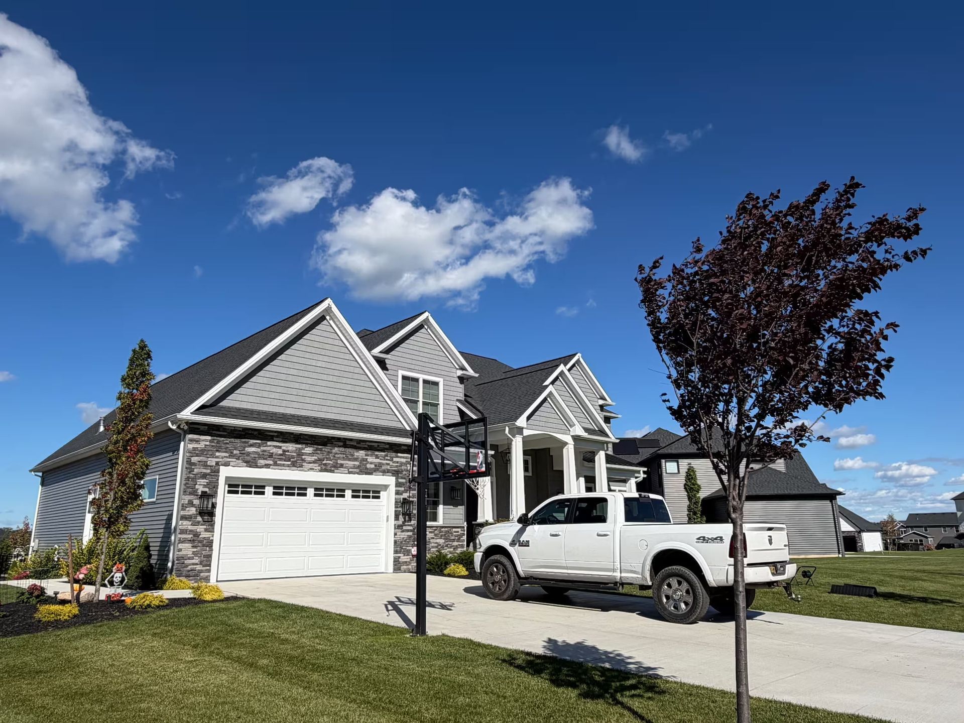Suburban house with gray siding, a white truck in the driveway, and a blue sky with clouds