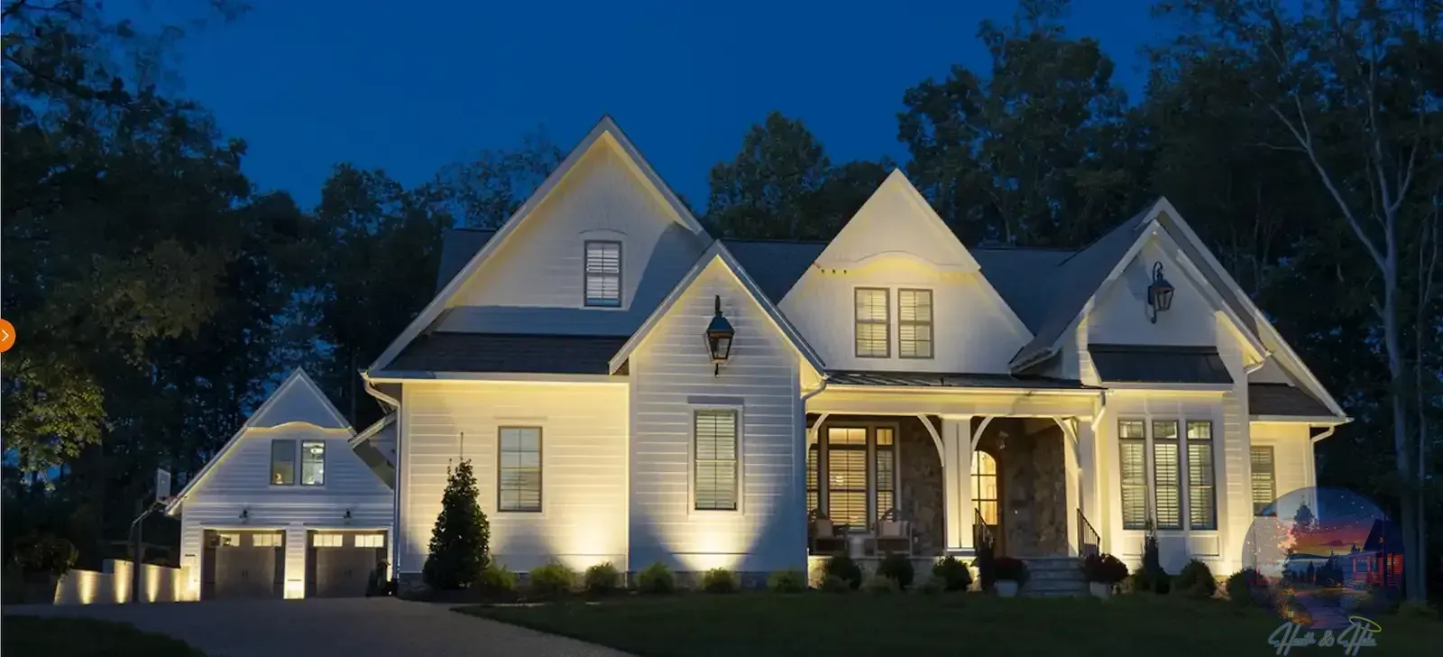 A modern farmhouse-style house at dusk with warm exterior lighting, a gabled roof, and a two-car garage.