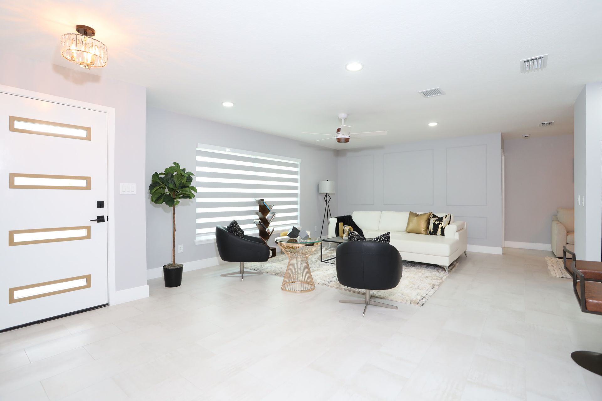 Bright modern living room with white sofa, black chairs, large window blinds, and a white front door