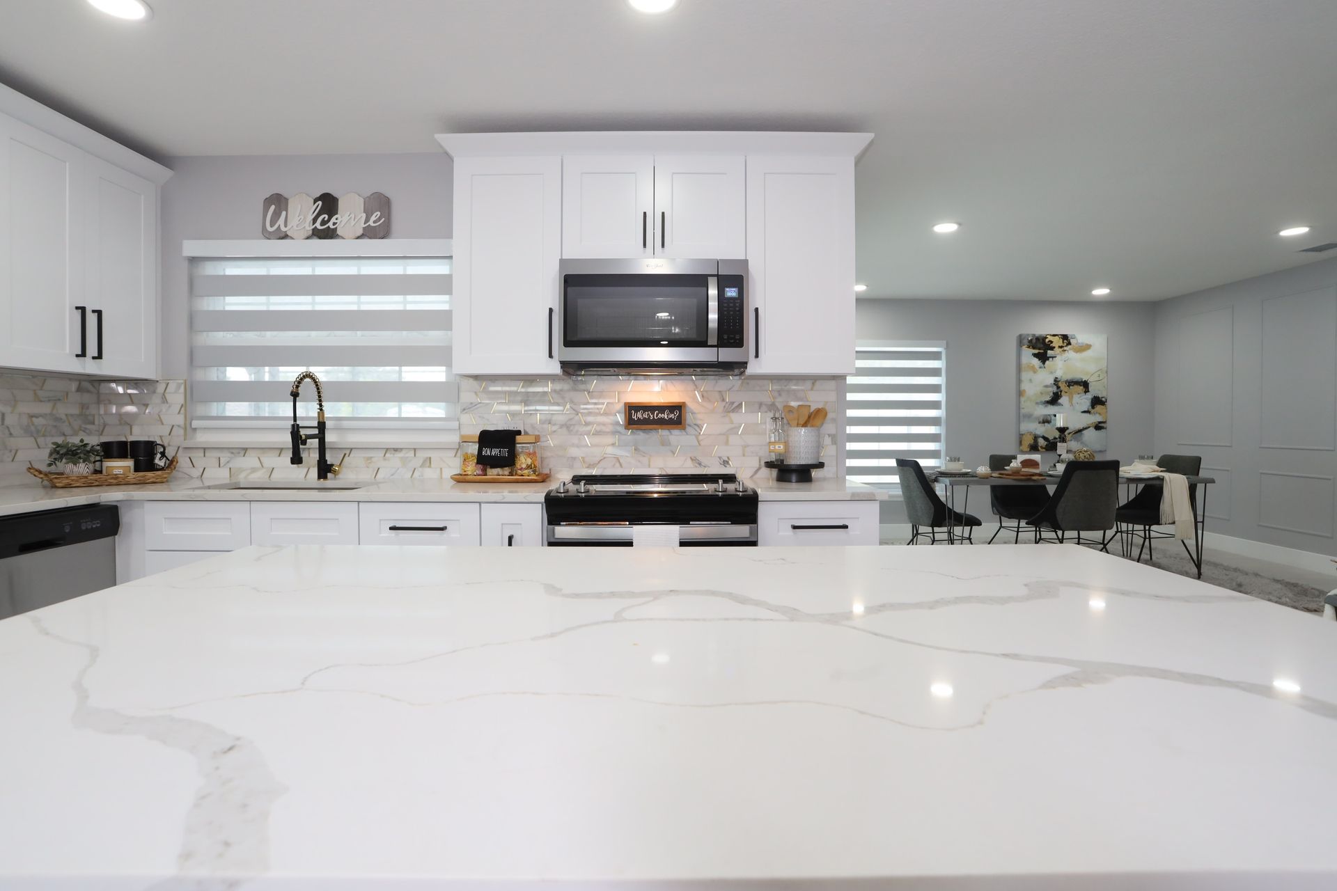 Bright modern kitchen with white cabinets, large island, stools, and pendant lights beside a dining area