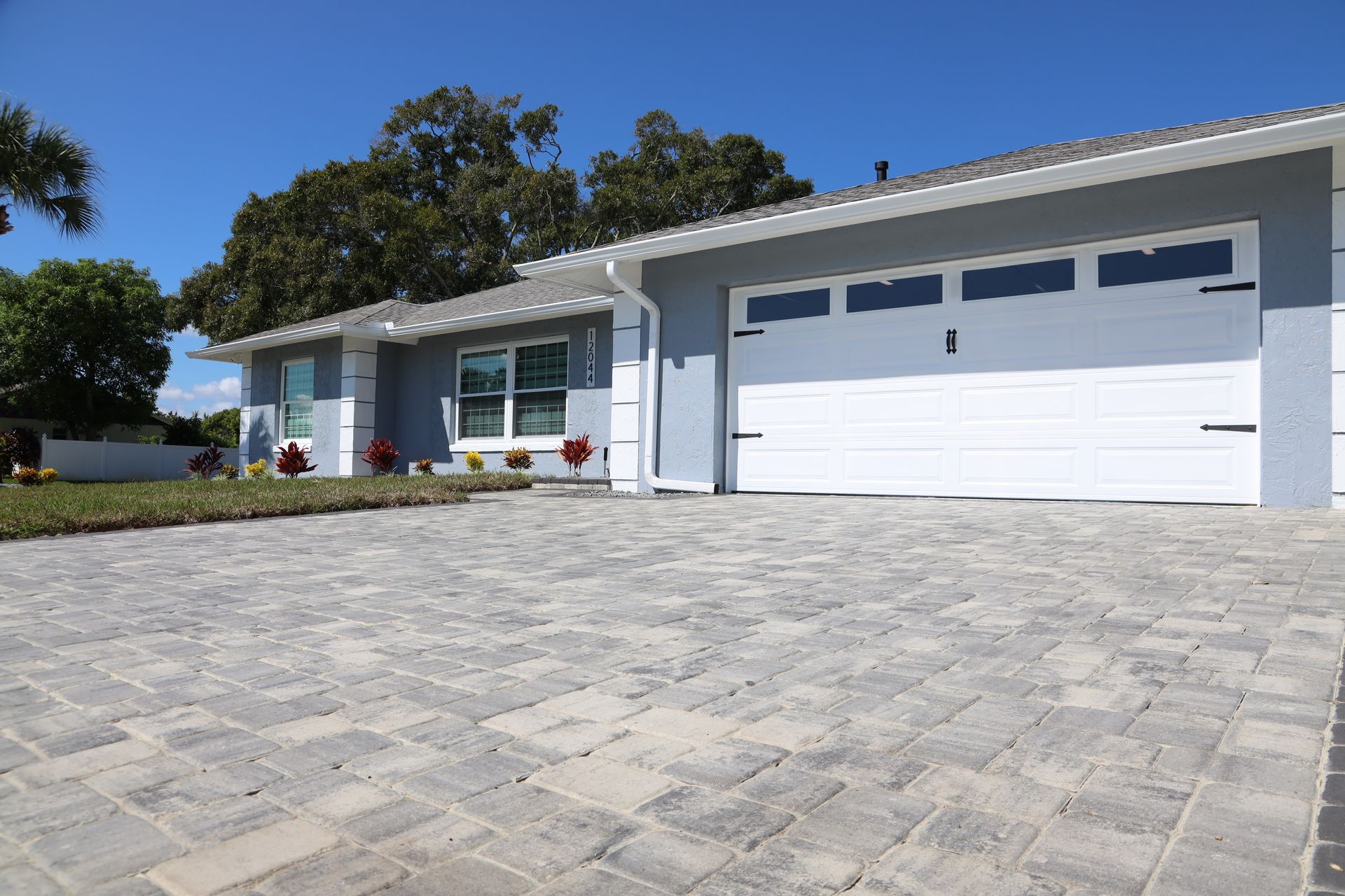 Modern single-story white house with a large garage and stone driveway under a blue sky